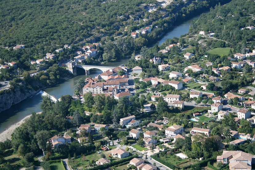 Vue aérienne de Ruoms en Ardèche, montrant le village entouré de nature et la rivière Ardèche