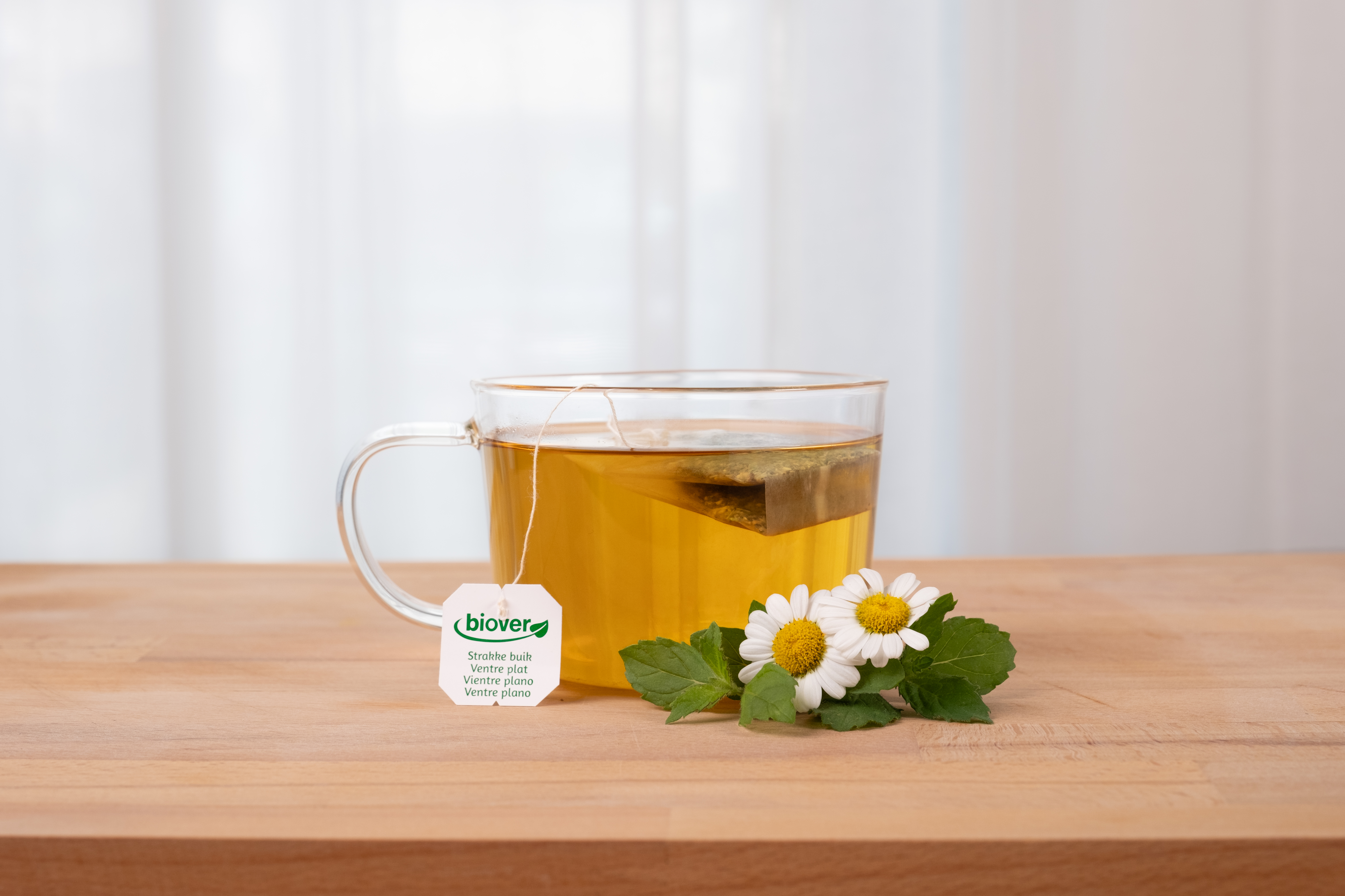 A transparent cup of yellow tea with a tea bag label reading "Biover" on a wooden table