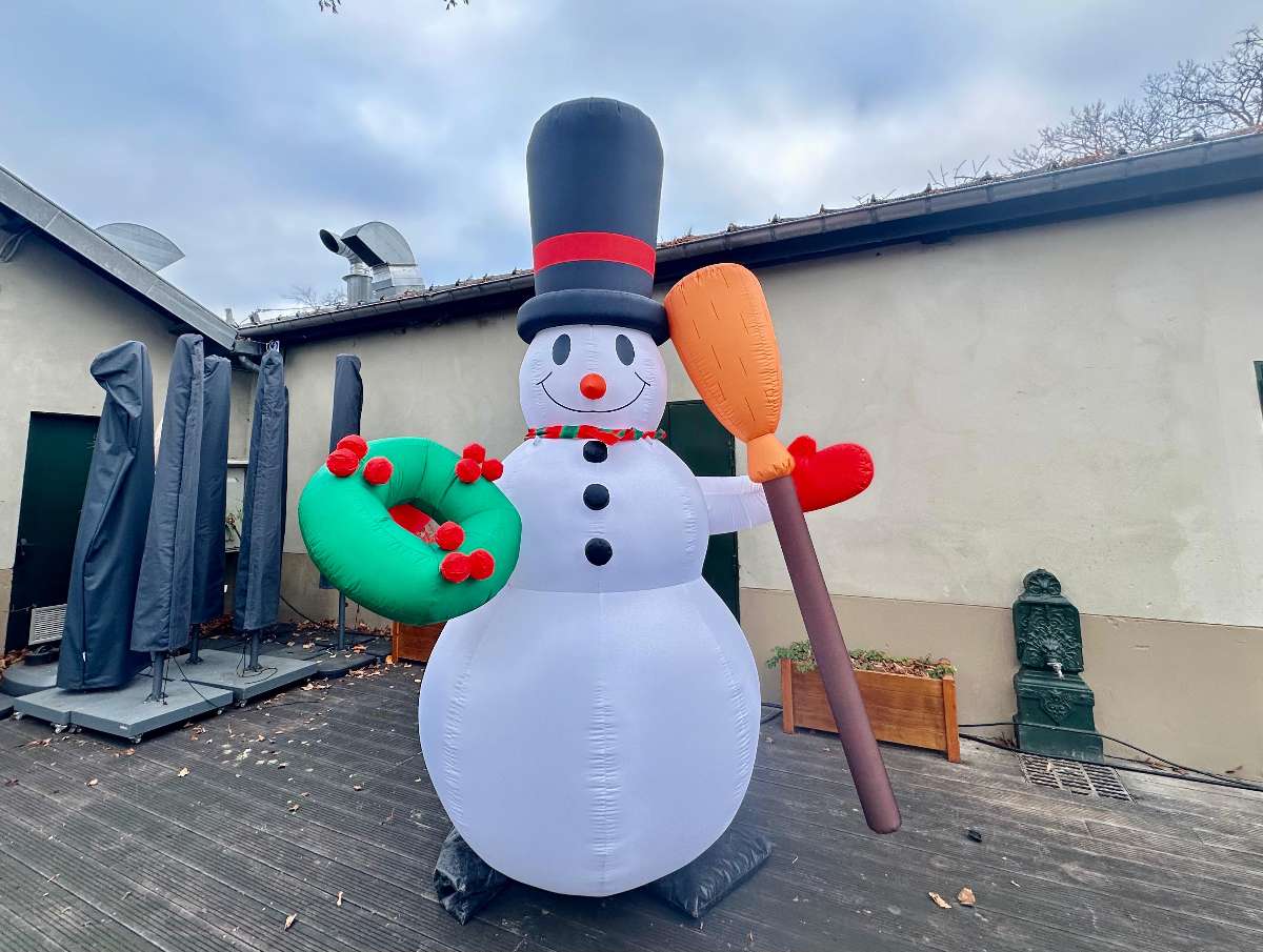 Décoration bonhomme de neige gonflable blanc avec un balais dans sa main gauche et un chapeau noir sur une terasse