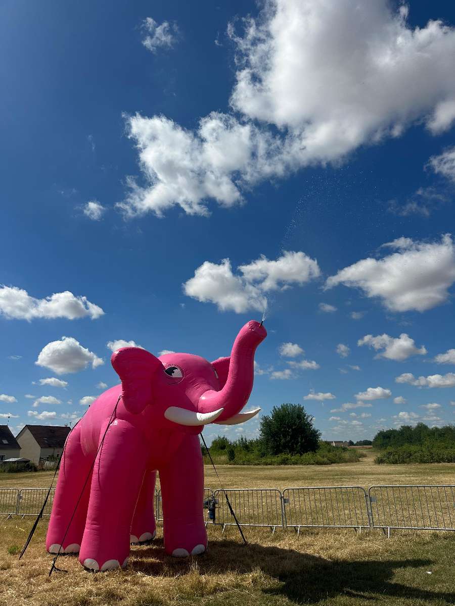 un éléphant Rose Gonflable brumisateur qui envoie de l'eau par la trompe avec un ciel bleu et légèrement nuageux