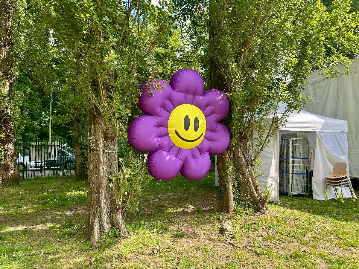fleur gonflable violette avec smiley jaune suspendu entre deux arbres à un mètre du sol
