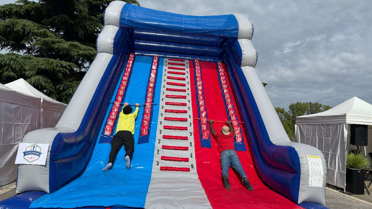 mur des champion interville gonflable avec deux personne qui grimpe a l'aide d'une barre en bois vue d'en bas 