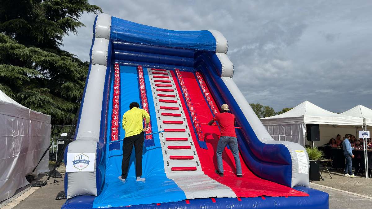 mur des champion interville gonflable avec deux personne qui grimpe a l'aide d'une barre en bois vue d'en bas 