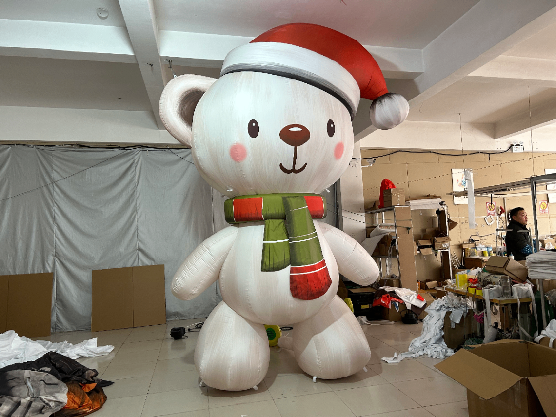Nounours géant gonflable avec un bonnet de noël rouge et une écharpe rouge et verte vue de trois quart