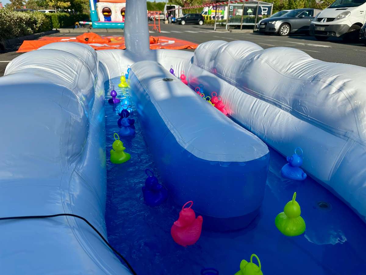 des canards avec des anneaux sur la tête  il sont multicolore et flottent à l'intérieur du bassin avec les parois blanche et le fond bleu