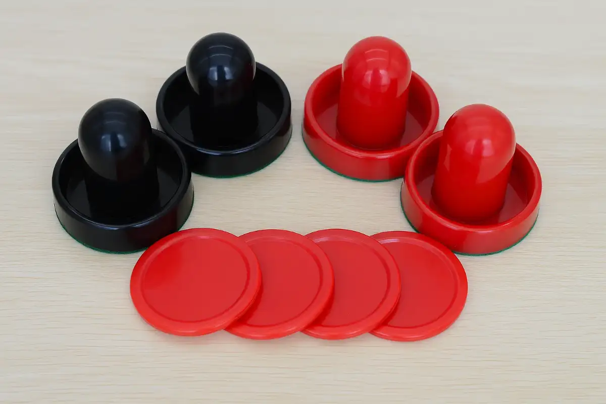 4 jetons de air hockey rouge et 2 poignets rouges et 2 poignets noires sur une table